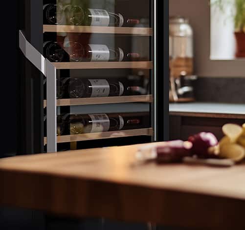 Une table en bois et une cave à vin noire vitrée avec 4 étagères.